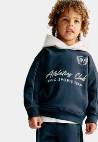 Marineblauwe sweatshirt met witte capuchonvoering, voorzien van de tekst 'Athletics Club' en 'Epic Sports Team', plus decoratieve stiksels op de mouwen.