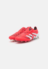Rode synthetische voetbalschoen met zwart-witte accenten, gestructureerde bovenkant, opvallende veters en conische noppen op een witte zool.