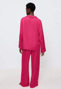 Fuchsia satin pyjamas med horisontella ränder, kraghalssnitt, långa ärmar och vida byxor med kontrasterande piping.