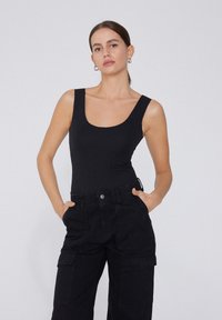 Zwart aansluitend bodysuit met een ronde halslijn, gecombineerd met zwarte cargobroeken met zakken en een losse snit. Matte stof, minimaal ontwerp.