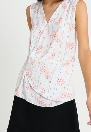 Blouse blanche sans manches avec des motifs floraux roses et des rayures verticales bleues, associée à une jupe noire.