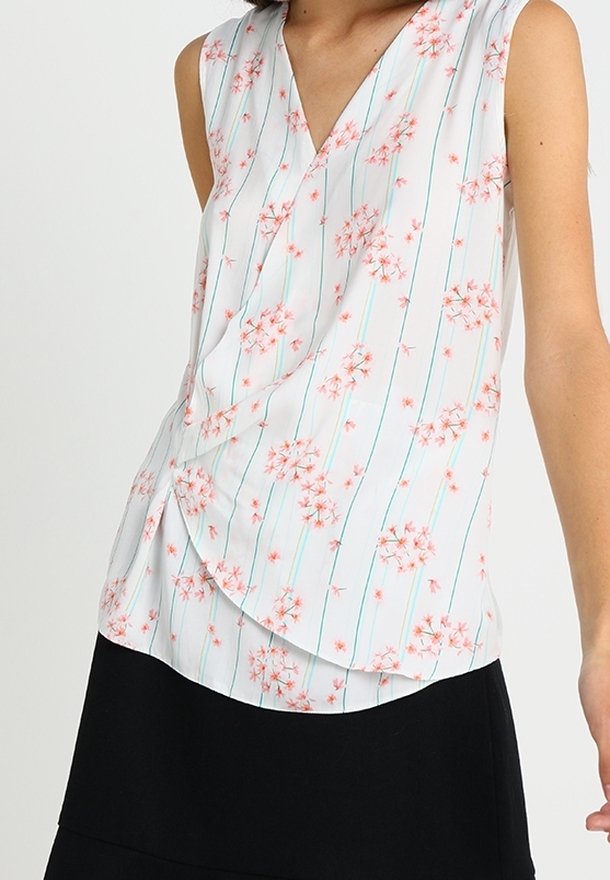 Blouse blanche sans manches avec des motifs floraux roses et des rayures verticales bleues, associée à une jupe noire.