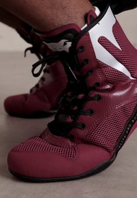 Sneaker alte rosse con pannelli in rete, lacci neri e accenti bianchi. La suola è testurizzata con una presa in gomma per garantire stabilità.