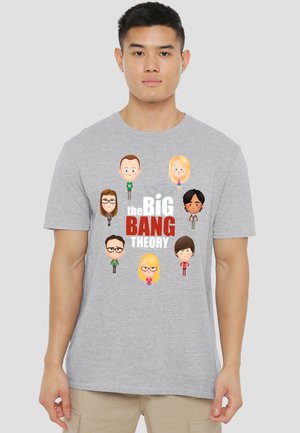 Young man wearing gray t-shirt with cartoon characters and text "The Big Bang Theory" on the front against a plain background.