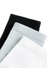 Stoh tri žíhaných ponožiek z pružnej tkaniny v čiernej, sivej a bielej farbe, prekrývajúcich sa a zobrazených z konca manžety na bielom pozadí.