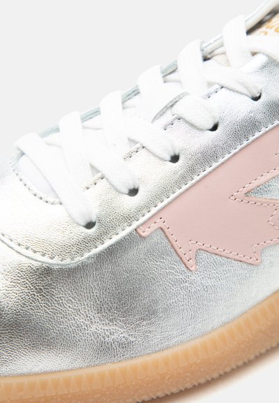 Baskets argentées avec lacets blancs, motif d'éclair rose sur le côté, et semelle en caoutchouc marron clair.
