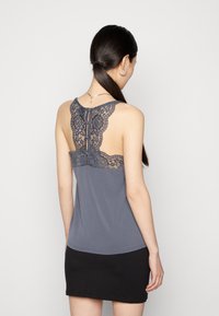 Débardeur gris avec un détail en dentelle dans le dos. Tissu doux avec une silhouette ajustée, présentant une ouverture en forme de clé à l'arrière. Design léger.