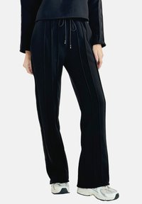 Pantaloni neri a vita alta con cordoncino, caratterizzati da una texture a righe verticali e gambe larghe e morbide. Abbinati a scarpe da ginnastica bianche.