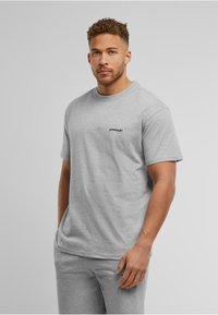 Graues Baumwoll-T-Shirt mit kurzen Ärmeln, Rundhalsausschnitt und kleinem schwarzen "UPSCale"-Logo auf der linken Brust. Legere Passform, glatte Textur.