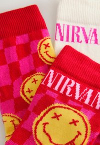 Bunte Socken mit einem karierten Muster in Pink und Rot, einem gelben Smiley-Gesicht und dem pinken Schriftzug "NIRVANA" auf der weißen Socke.