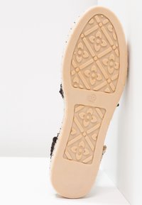 Semelle d'une chaussure beige avec des motifs géométriques et floraux, taille 39 visible au centre.