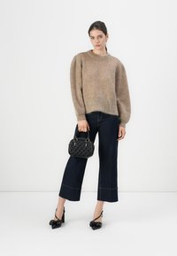 Maglione beige lavorato a maglia con maniche a palloncino, pantaloni larghi in denim scuro e una borsa nera testurizzata di piccole dimensioni; scarpe nere con tacco alto.
