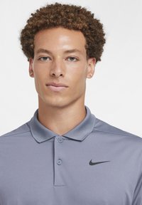 Gray polo shirt with a collar and two buttons, featuring a black Nike logo. Smooth fabric texture with a classic design.