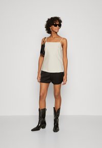 Light beige camisole with thin straps, paired with black shorts. Sheer fabric and smooth texture. Black pointed-toe boots and small black bag.