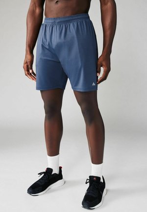 Shorts de sport bleu marine avec une ceinture élastique et un tissu texturé, accompagnés de baskets noires et de chaussettes blanches. Présente des détails de logo.