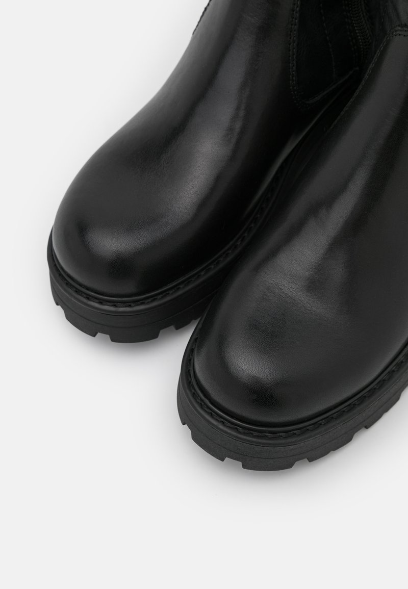 Bottes en cuir noir avec une finition lisse, bout arrondi et semelle en caoutchouc épaisse avec un motif de traction texturé.