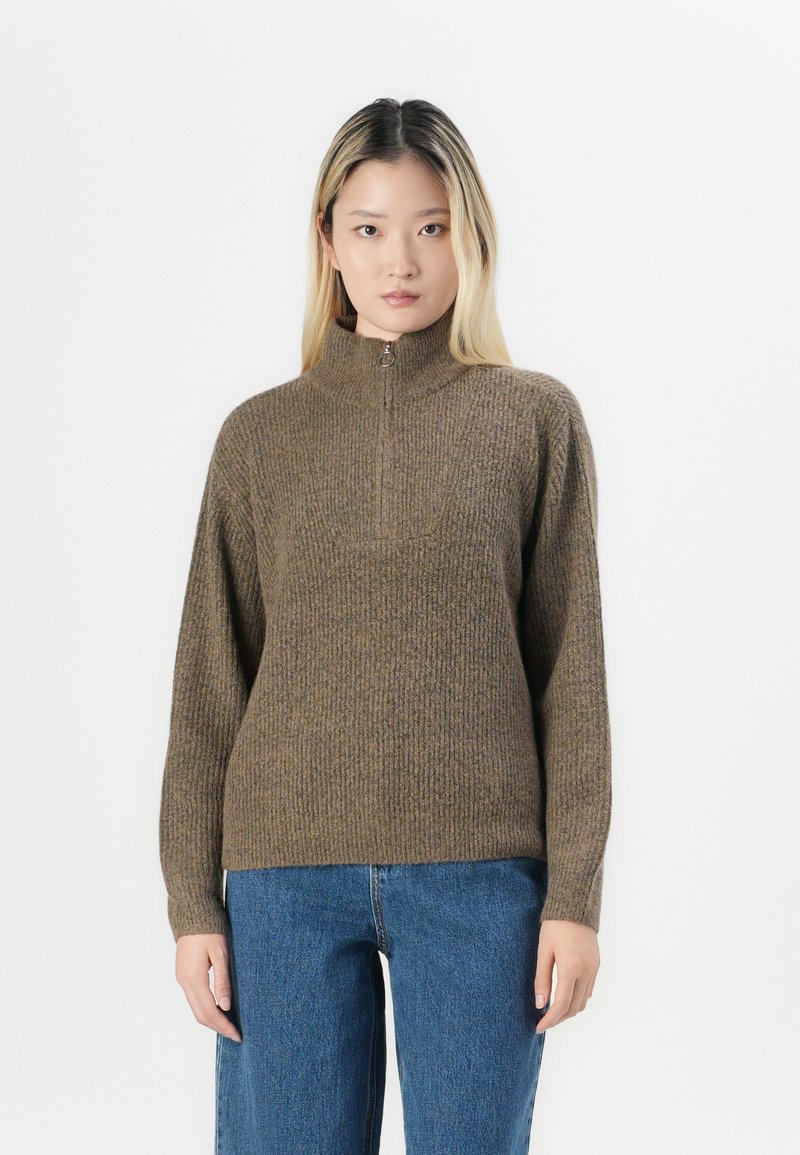 Maglione marrone a coste con colletto alto e dettaglio a mezza zip, abbinato a jeans blu in denim dall'aspetto rilassato. Tessuto morbido e vestibilità comoda.