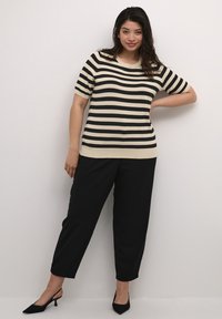 Sort og kremfarvet stribet kortærmet top parret med sorte slim-fit bukser og sorte hæle. Stoffet virker glat og let.