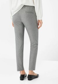 Graue schmal zulaufende Hosen aus dehnbarem Material, mit einer Gesäßtasche und einem glatten Bund. Getragen mit schwarzen Ballerinas.