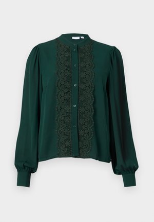 Blusa verde oscura con cuello alto y mangas largas. Presenta un panel de encaje en la parte frontal, complementado con botones y una textura suave.