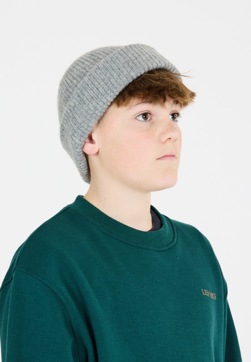 Grijze gebreide beanie met een geribde textuur; gedragen met een groene sweatshirt met een ronde hals en een klein gouden logo op de borst.
