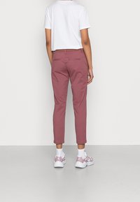 Różowe bawełniane spodnie z wąskimi nogawkami, z paskami na pasek i tylnymi kieszeniami, w połączeniu z białymi trampkami i krótkim białym T-shirtem.