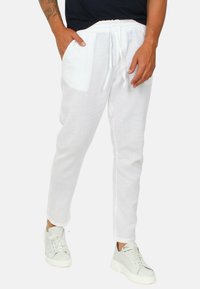 Pantaloni jogger bianchi in lino con vita regolabile con cordino, tasche laterali e vestibilità rilassata, abbinati a sneaker grigie.