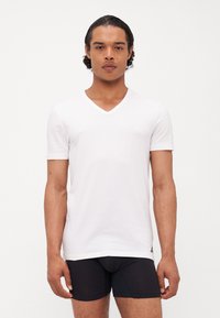 Weißes kurzärmliges V-Neck T-Shirt aus weichem Stoff, taillierte Passform, mit minimalem Branding unten links.