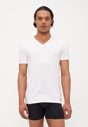 T-shirt blanc à manches courtes en V, fabriqué en tissu doux, design ajusté, avec un branding minimal en bas à gauche.