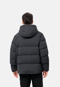 Veste matelassée noire avec capuche, présentant un design cousu et des poignets élastiques, vue de l'arrière. Texture lisse et forme compacte.