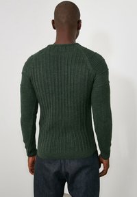 Donkergroene geribbelde gebreide trui met lange mouwen, aangesloten pasvorm en raglannaden, met een gestructureerde stof en een ronde hals.