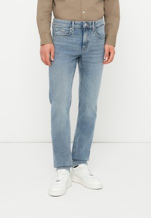 Jean en denim bleu clair avec une coupe droite, un design à cinq poches, des accessoires en métal et des détails de couture discrets, portés avec des baskets blanches.