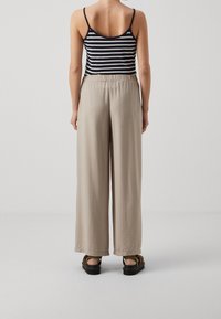 Ljusbeige vida byxor med elastisk midja, parat med en marinblå och vit randig tanktopp, sedd bakifrån.