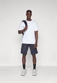 White short-sleeve t-shirt with a chest pocket, paired with navy shorts featuring zippered pockets, and white sneakers with gray soles.