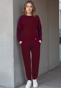 Bordeaux sweatshirt en bijpassende joggers van zachte stof, met ribgebreide manchetten en een klein logo-accent, gecombineerd met witte sneakers.