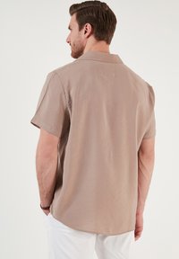 Kortærmet skjorte med krave i lysebeige stof, der har en afslappet pasform og en synlig rygsøm detalje. Enkelt design uden mønstre.