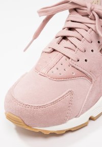 Närbild av rosa mockasneakers med matchande snörning, perforerade detaljer och gummisulor på en vit bakgrund.