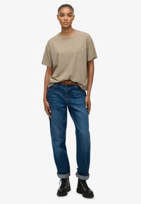 Beige bomulds t-shirt, der er parret med blå denim jeans, prydet med et vævet brunt bælte og sorte snørestøvler med en kraftig sål.