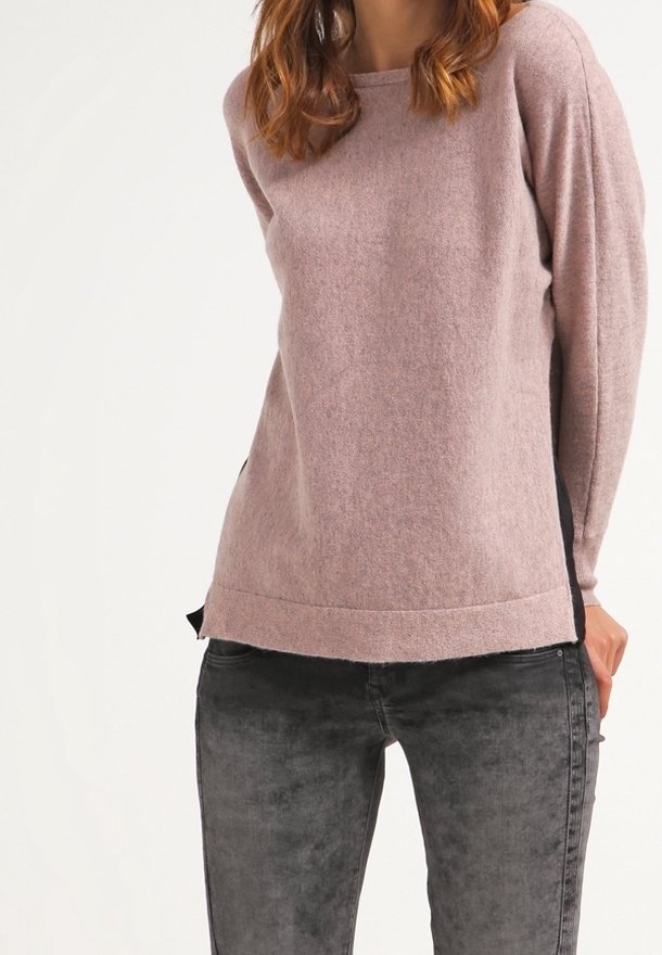 Långärmad pullover i ljusrosa ullblandning; har en rundad halsringning och kontrasterande svarta sidopaneler; mjuk textur. Grå tajta jeans.