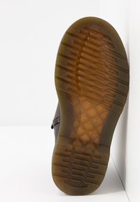 Brązowy gumowy bieżnik z teksturowanym wzorem antypoślizgowym. Przezroczysta część obcasa z widoczną wewnętrzną strukturą. Lekki połysk i zaokrąglone krawędzie.