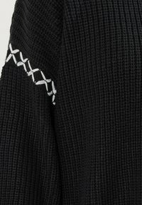 Maglione nero lavorato a maglia caratterizzato da un motivo testurizzato e accenti bianchi cuciti lungo la spalla. Nessun richiamo visibile o ulteriori abbellimenti.