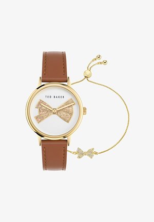 Braunlederarmbanduhr mit Gehäuse in Goldtönen. Das weiße Ziffernblatt hat ein glitzerndes Schleifenmuster. Seitliche Kette mit einem kleinen Strass-Schleifenakzent.