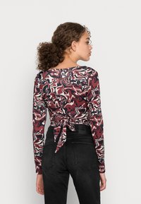 T-shirt de manga longa com um padrão abstrato multicolorido em tons de bordô, preto e branco, apresentando uma fita nas costas e um decote arredondado.
