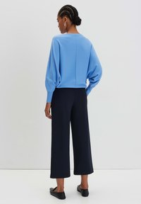 Maglione azzurro chiaro lavorato a maglia con scollo rotondo e maniche a palloncino, abbinato a pantaloni larghi blu navy e scarpe slip-on nere.