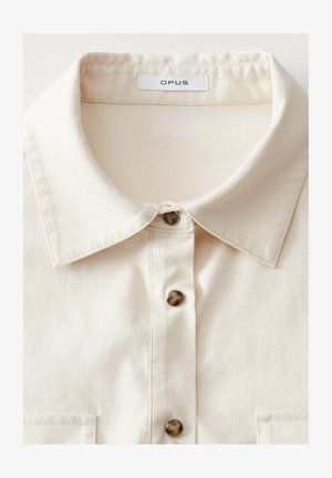 Camicia crema con colletto strutturato, dotata di cinque bottoni marroni scuri e una tasca sul petto, realizzata in un tessuto liscio.