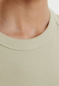 Débardeur côtelé vert clair avec un col rond et une texture lisse et douce. Gros plan mettant en valeur les fines lignes du tissu.