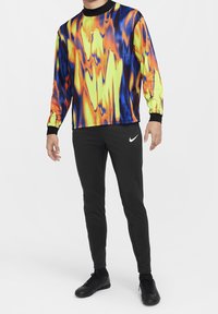 Kolorowa, długorękawowa koszulka sportowa z wirującym wzorem w czerwieni, pomarańczu, żółci i niebieskim; zestawiona z dopasowanymi czarnymi spodniami i butami.