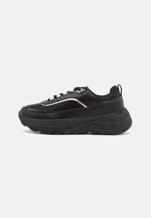 Sort chunky sneaker med tyk sål, mesh og læder overdel, snørebånd foran og trækflig ved hælen, vist i sideprofil på hvid baggrund.