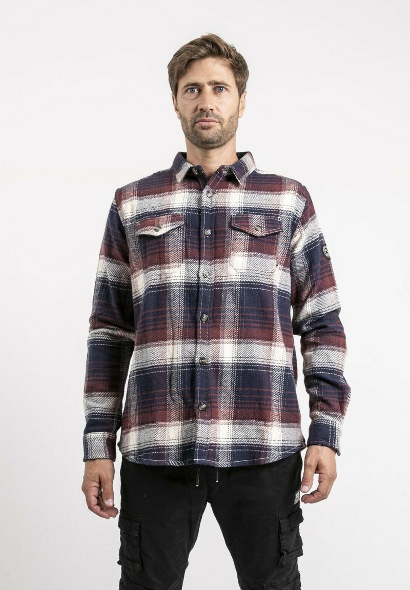 Chemise en flanelle à carreaux avec des couleurs rouge, marine et blanche. Caractéristiques : fermeture à boutons sur le devant, deux poches poitrine et manches longues. Tissu texturé.