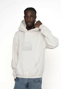 Hedvábná mikina v off-white barvě s přední kapsou, která nese vyšívané logo "MM multiply apparel". Měkká látka, uvolněný střih, žebrované manžety a spodní lem.